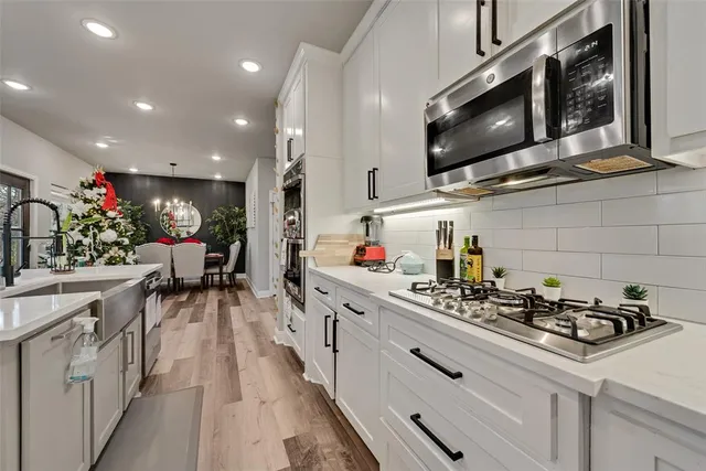 a kitchen with stainless steel appliances kitchen island granite countertop a sink dishwasher a microwave oven a stove and white cabinets with wooden floor