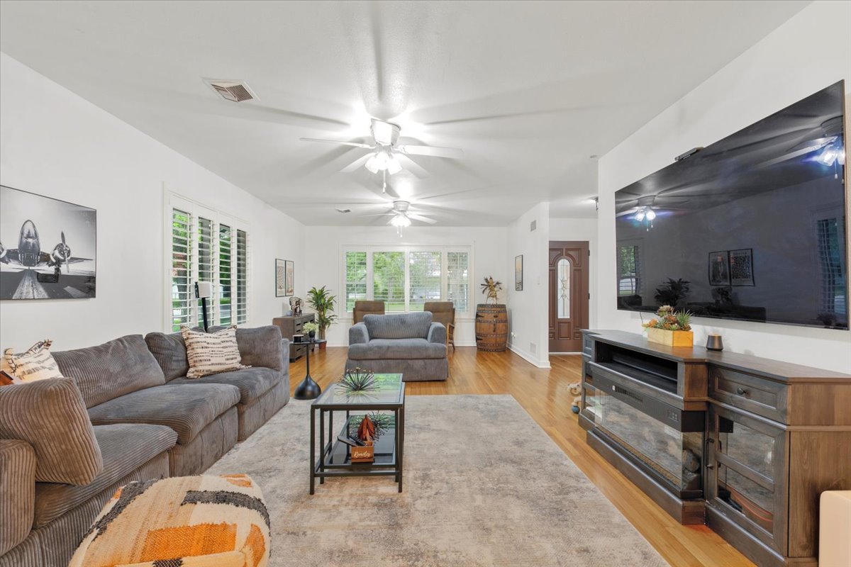 607 Short Street Smithville, TX 78957 - Photo 4 of 31 Spacious living area featuring wood-finish flooring, white walls, multiple ceiling fans, and large windows with plantation shutters
