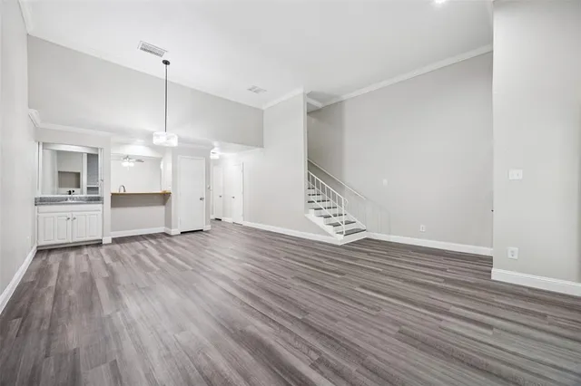 a view of an empty room with wooden floor and a kitchen