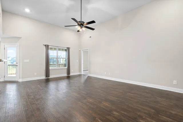 an empty room with wooden floor fan and windows
