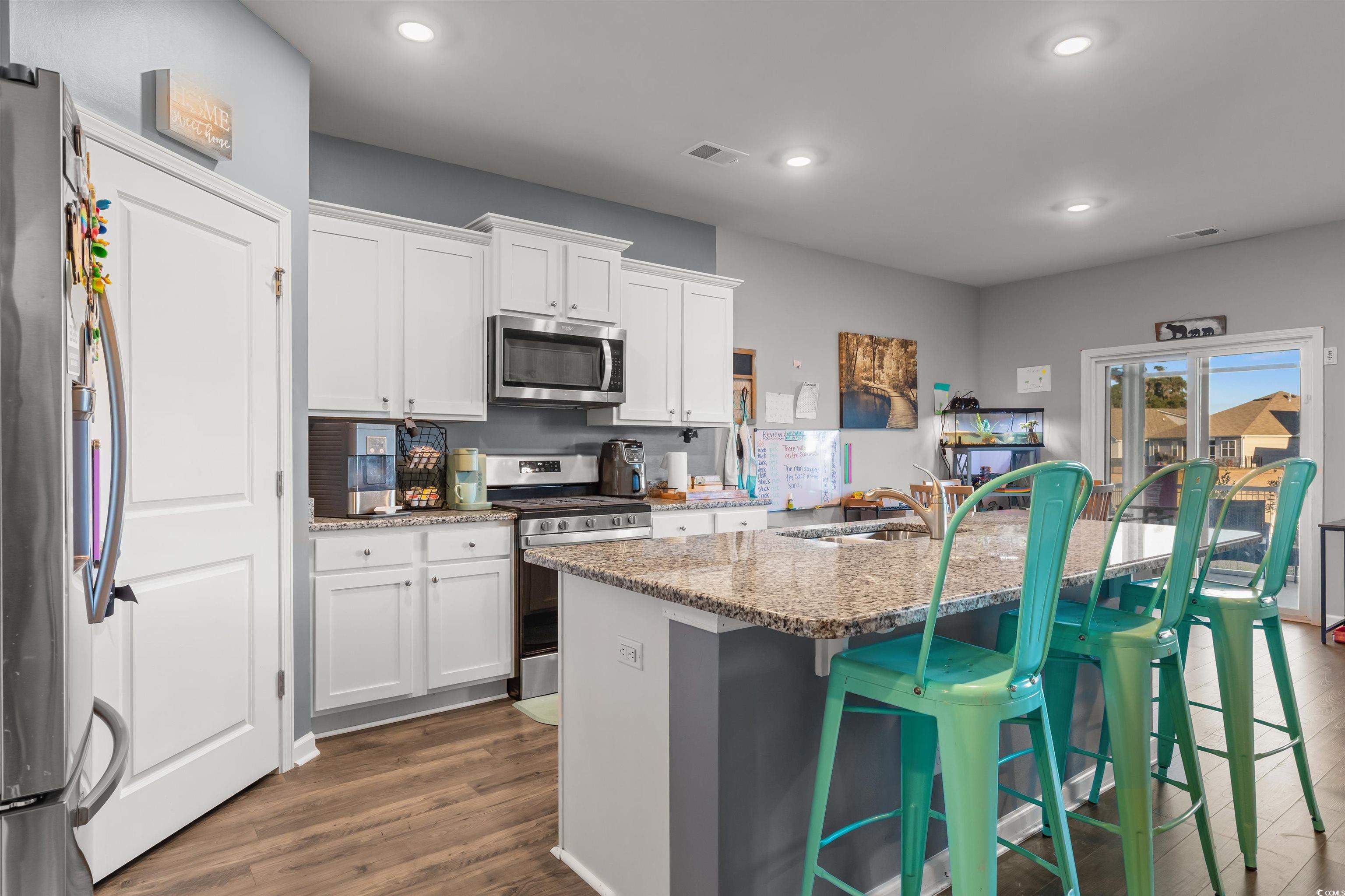 2004 Musgrove Mill Way Myrtle Beach, SC 29579 - Photo 4 of 35 Kitchen featuring a kitchen breakfast bar, light stone countertops, stainless steel appliances, dark wood-style floors, and white cabinets