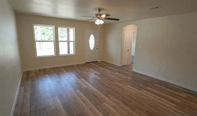 an empty room with wooden floor chandelier fan and windows