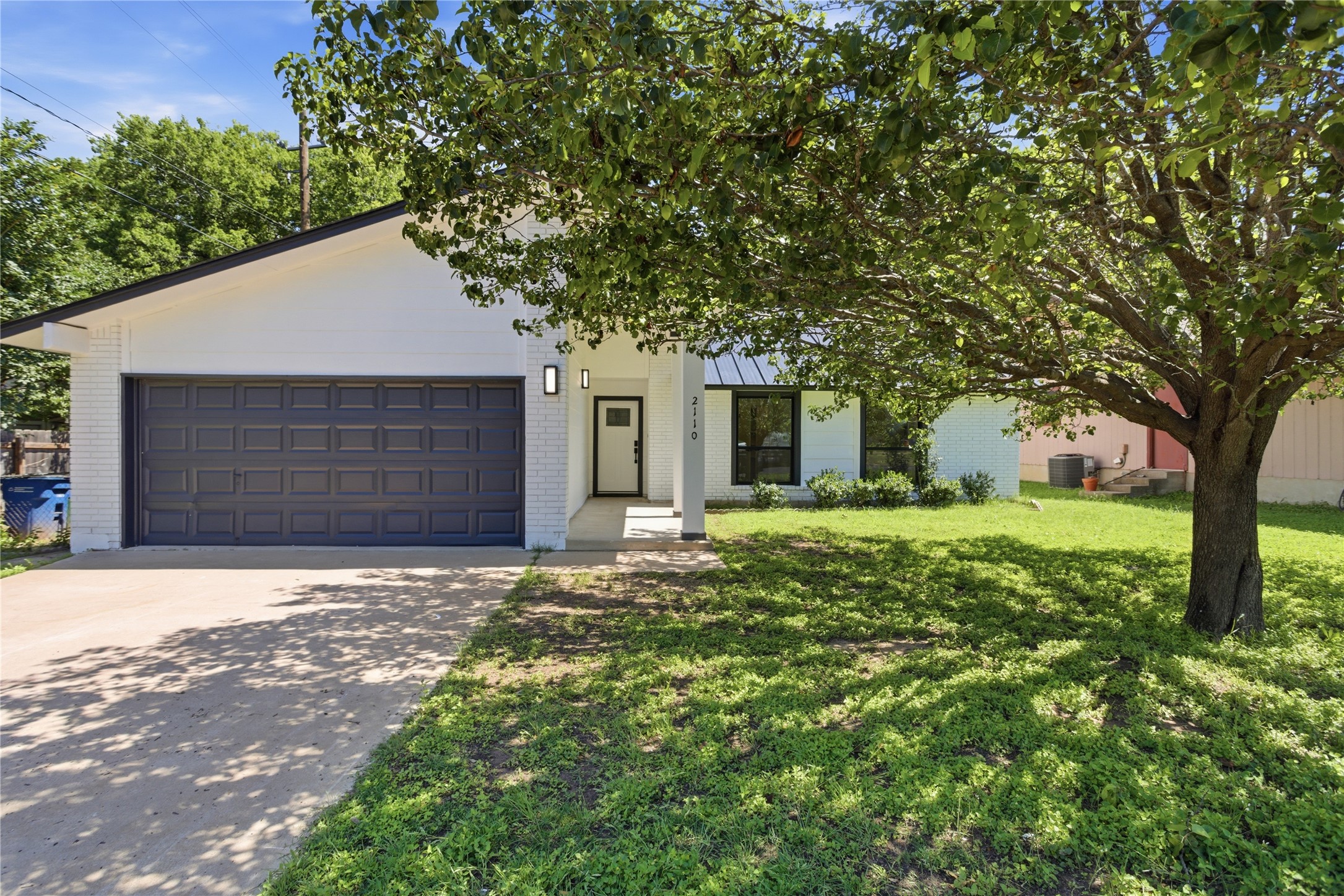 2110 Magazine Street Austin, TX 78727 - Photo 1 of 31 Front exterior featuring a dark gray garage door, white brick accents, concrete driveway, and a mature tree
