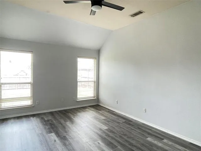 an empty room with wooden floor fan and windows