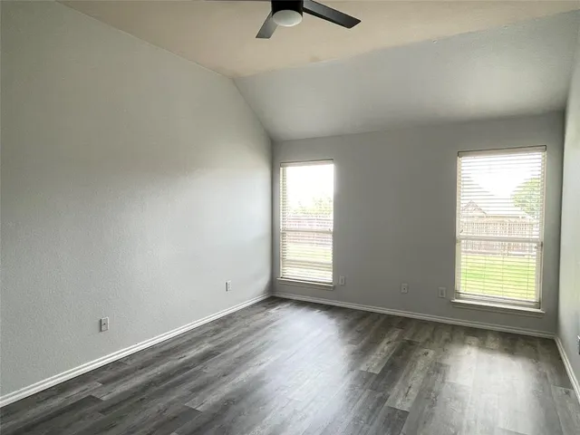 an empty room with wooden floor fan and windows