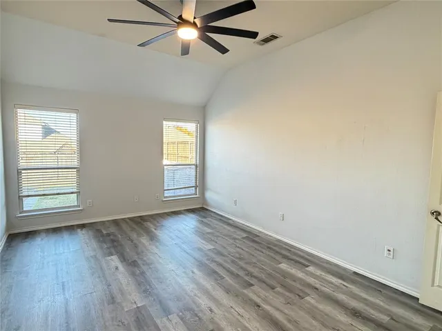 an empty room with wooden floor fan and windows