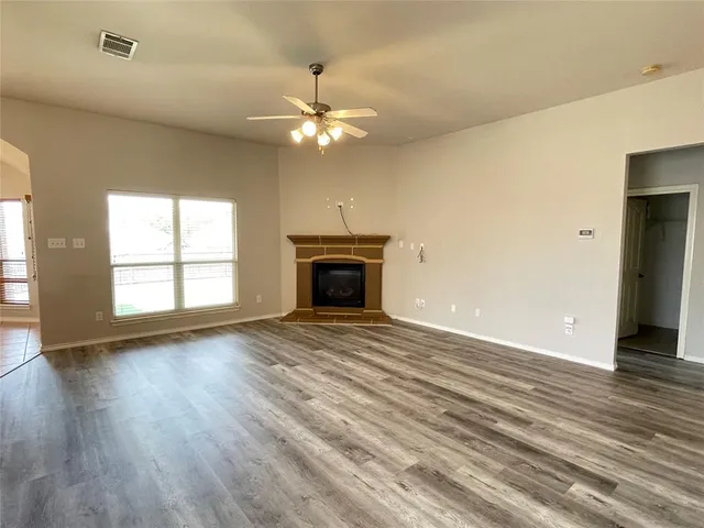 an empty room with wooden floor ceiling fan and windows