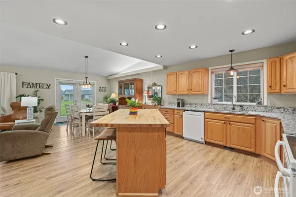 a open kitchen with stainless steel appliances granite countertop a stove top oven a refrigerator a dining table and chairs with wooden floor