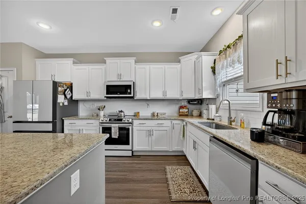 a kitchen with stainless steel appliances granite countertop a stove top oven a sink a refrigerator and white cabinets