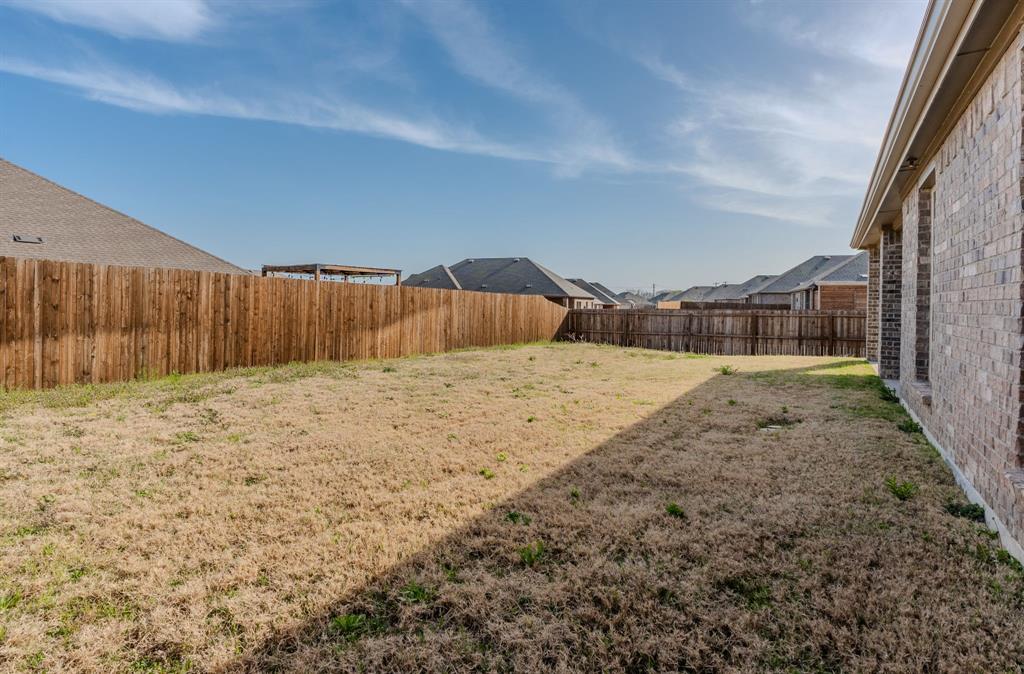2902 Trusting Way Aubrey, TX 76227 - Photo 36 of 38 Expansive rear yard featuring a wood privacy fence, a brick exterior, and a visible neighborhood roofline