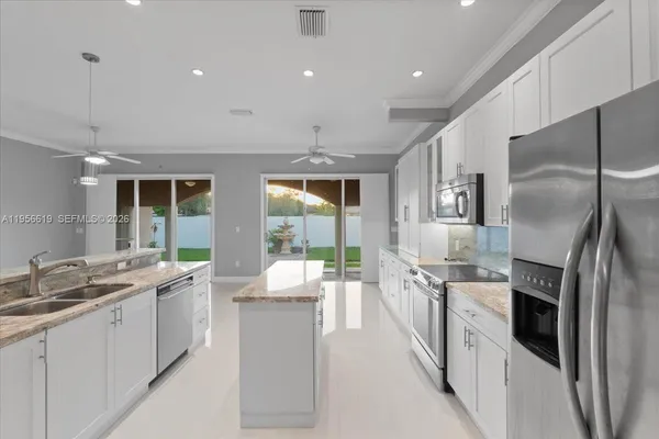 a large kitchen with stainless steel appliances kitchen island a large counter tops a white cabinets and couches