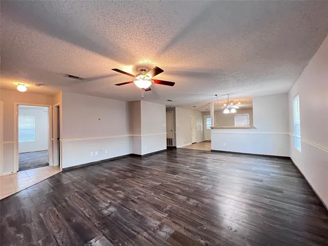 an empty room with wooden floor chandelier fan and windows
