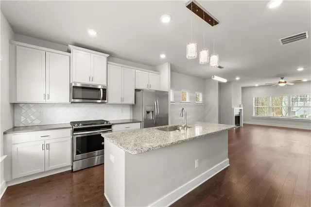 a large kitchen with stainless steel appliances kitchen island granite countertop a stove a sink dishwasher and a refrigerator with wooden floor