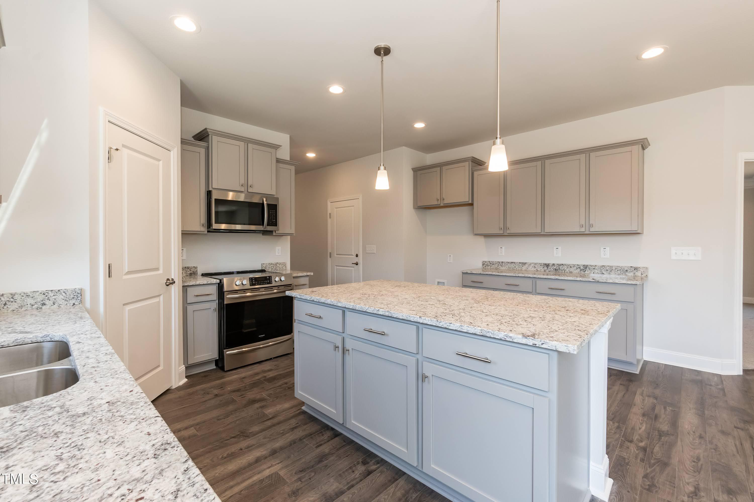 45 High Hampton Way Fuquay-Varina, NC 27526 - Photo 11 of 43 a kitchen with kitchen island granite countertop a stove a sink a refrigerator and white cabinets with wooden floor