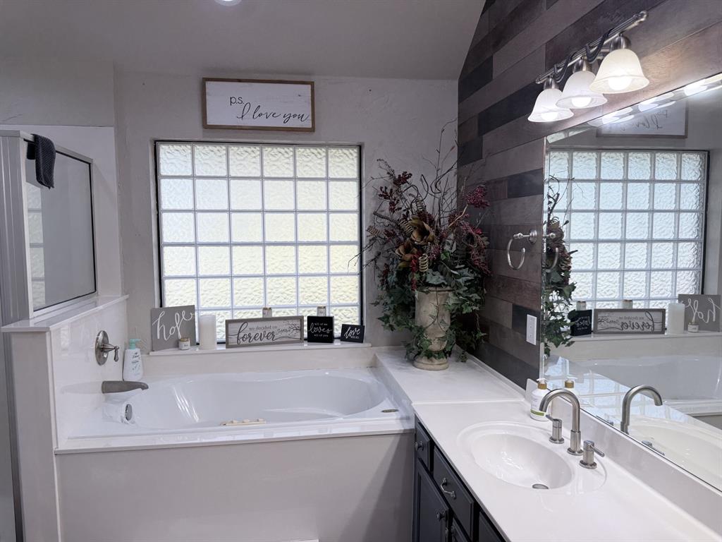 313 An County Road, Unit 2145 Palestine, TX 75801 - Photo 24 of 40 Built-in soaking tub, privacy glass block window, dual vanity with undermount sinks, wood-finish accent wall, and integrated vanity lighting