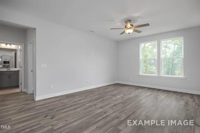 an empty room with wooden floor chandelier fan and windows