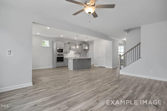 a view of an empty room with wooden floor and a kitchen