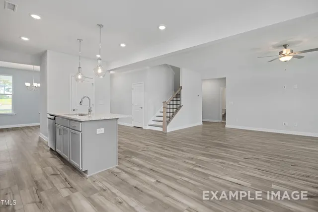 a view of an empty room with wooden floor and a kitchen
