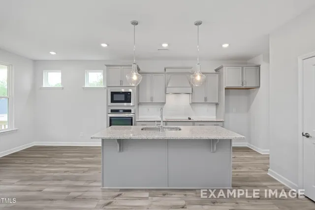 a large kitchen with kitchen island a stove a sink dishwasher and a oven with wooden floor