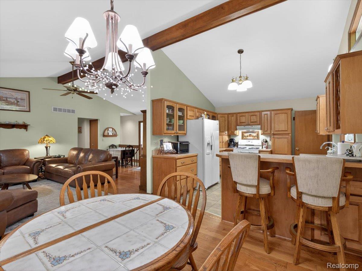 9714 Naiad Road Clarkston, MI 48348 - Photo 21 of 61 Open-concept kitchen and dining area featuring natural wood cabinetry, a breakfast bar, and a vaulted ceiling with exposed wood beams.