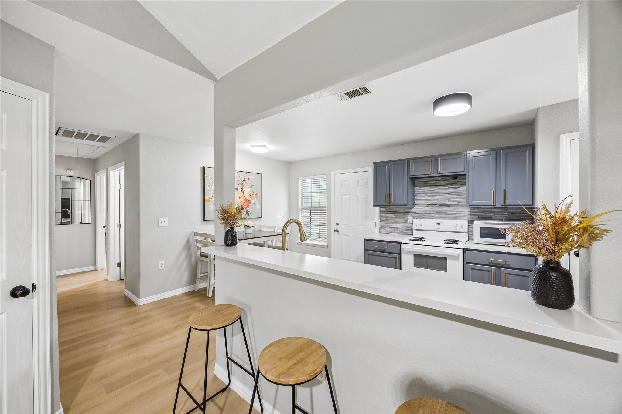 539 Anderson Street Sealy, TX 77474 - Photo 11 of 19 Modern kitchen with stylish blue cabinets, a sleek tile backsplash, and white countertops. The space includes a bar area with seating, wood floors, and a bright, open layout with plenty of natural light.