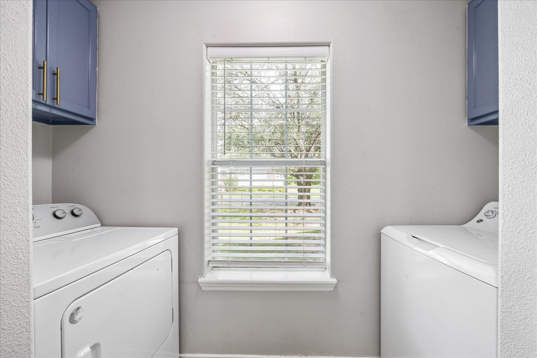 539 Anderson Street Sealy, TX 77474 - Photo 16 of 19 The laundry room features a window for natural light, upper cabinets in a stylish blue color with brass handles.