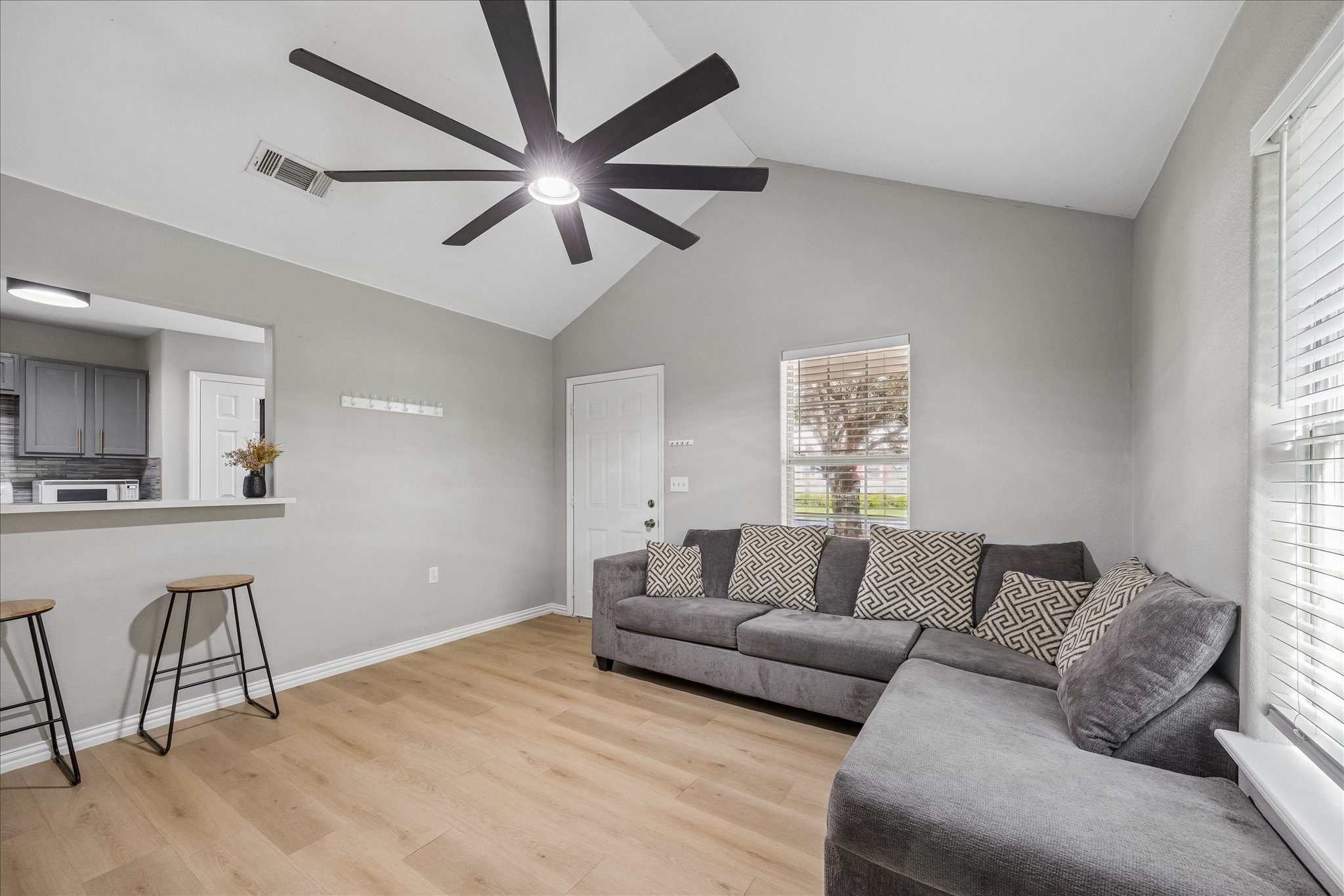 539 Anderson Street Sealy, TX 77474 - Photo 7 of 19 Spacious living space with light wood flooring and neutral walls. High vaulted ceiling with a contemporary fan, and a breakfast bar with space for seating. Ample natural light comes through the windows, creating a bright and inviting atmosphere.