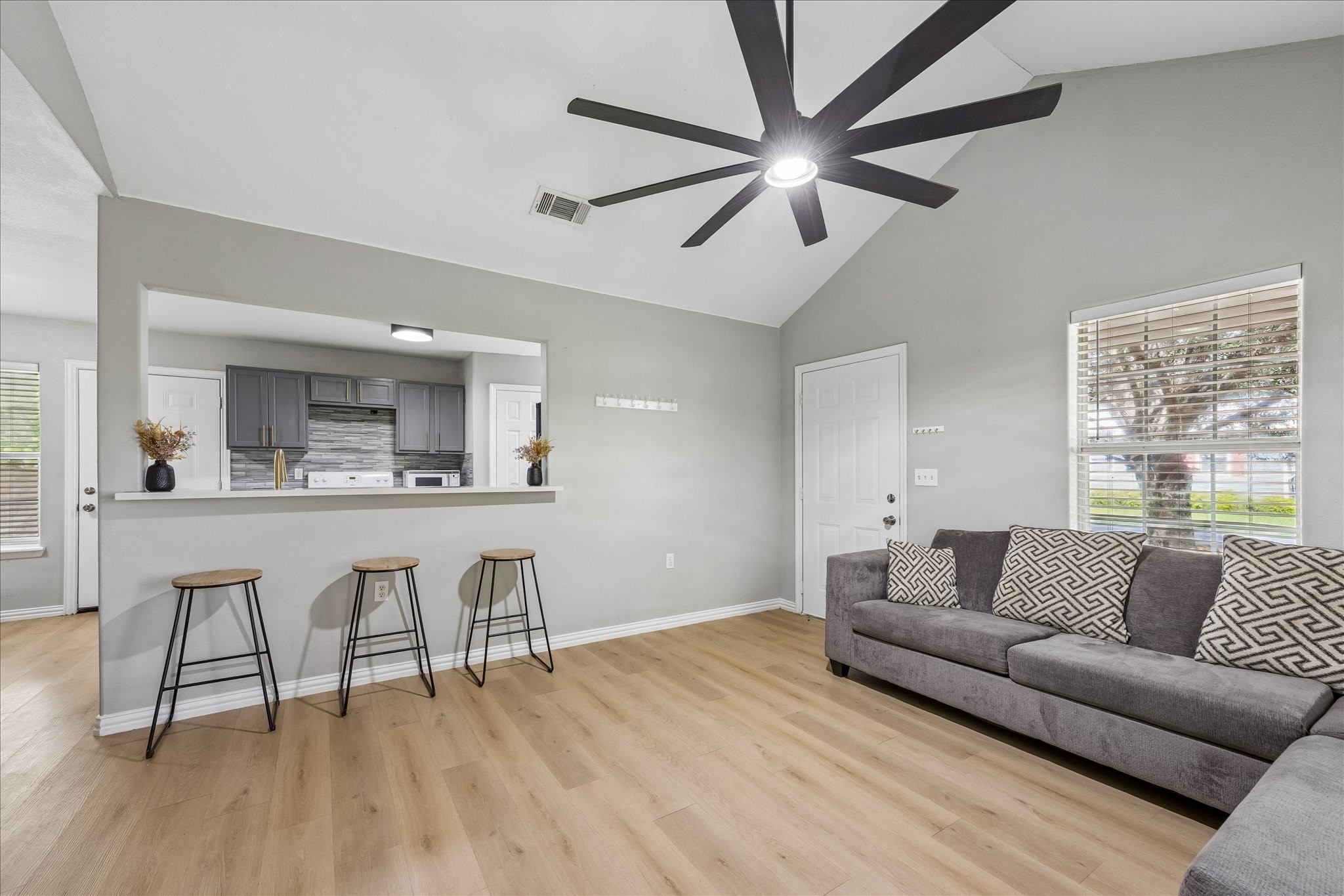 539 Anderson Street Sealy, TX 77474 - Photo 8 of 19 Spacious living space with light wood flooring and neutral walls. High vaulted ceiling with a contemporary fan, and a breakfast bar with space for seating. Ample natural light comes through the windows, creating a bright and inviting atmosphere.