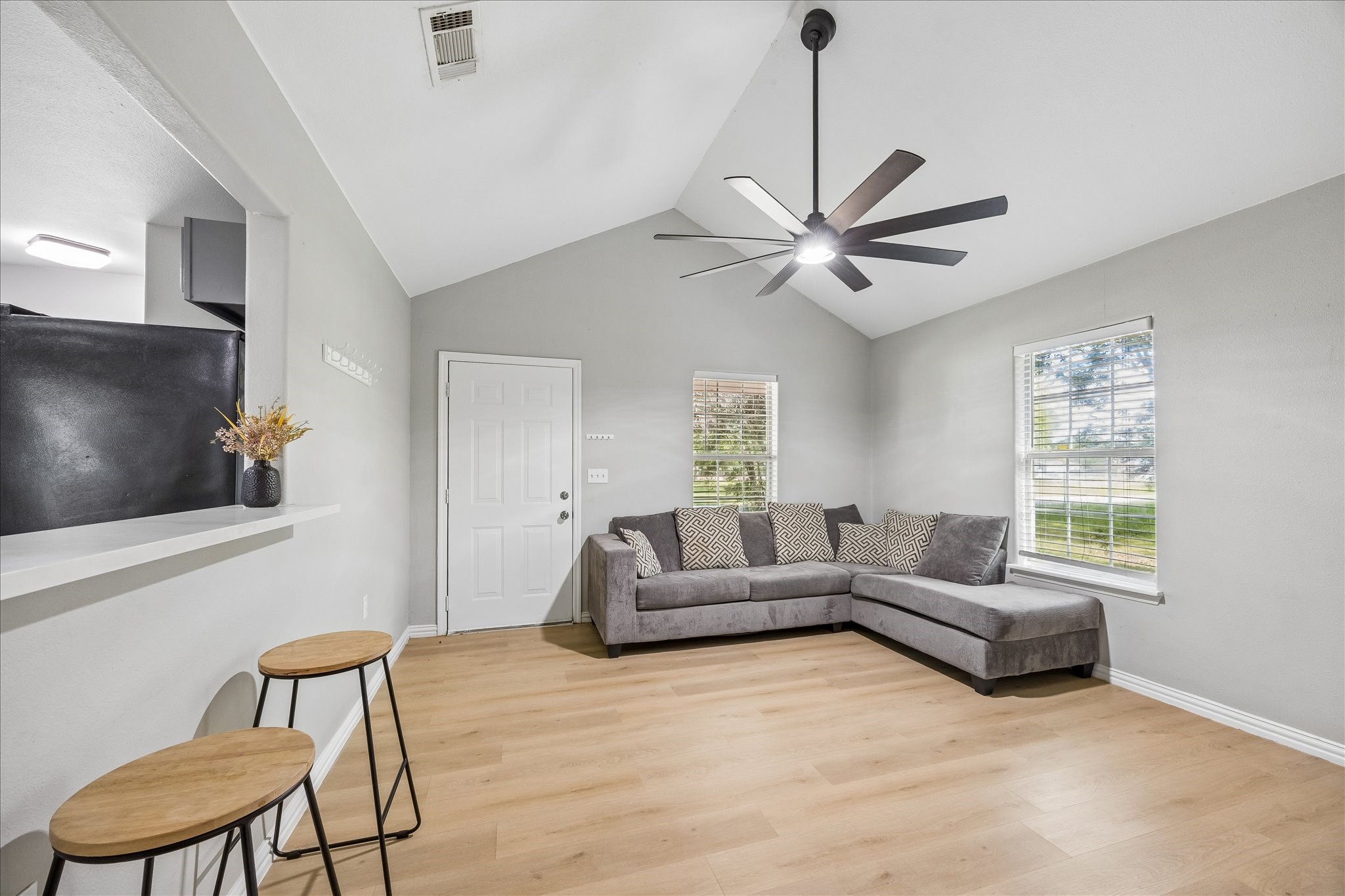 539 Anderson Street Sealy, TX 77474 - Photo 9 of 19 Bright, modern living room with light wood flooring, large windows providing ample natural light. The space features a high ceiling with a sleek ceiling fan, and there's an open bar area with space for seating offering a seamless flow into the kitchen.