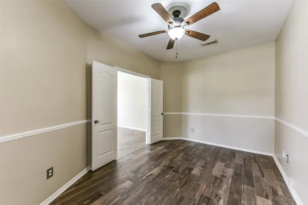 an empty room with wooden floor chandelier fan and windows
