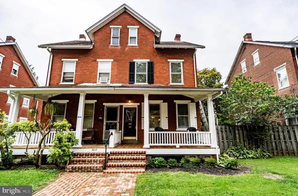 a view of a brick house with a yard plants and large tree