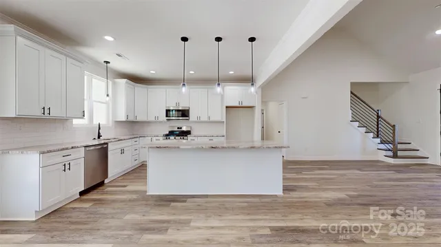 a large kitchen with stainless steel appliances granite countertop a stove a sink dishwasher a refrigerator white cabinets and wooden floor