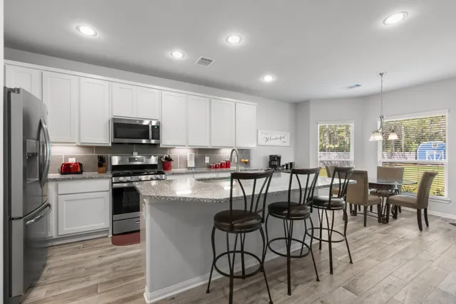 a view of kitchen with stainless steel appliances granite countertop dining table chairs refrigerator microwave and cabinets