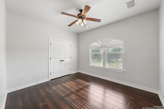an empty room with wooden floor chandelier fan and windows