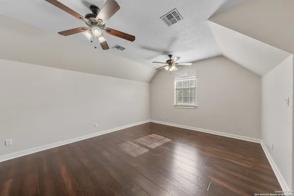 an empty room with wooden floor fan and windows