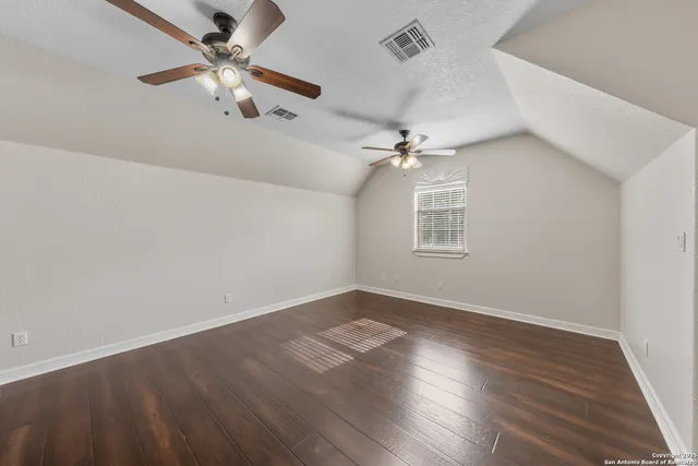 an empty room with wooden floor fan and windows