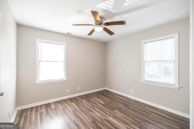 an empty room with wooden floor windows and fan