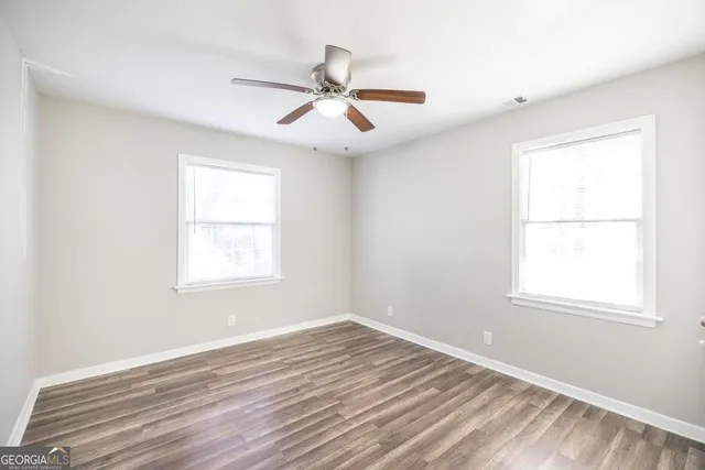 an empty room with wooden floor windows and fan