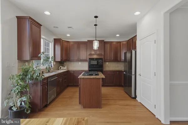 a kitchen with kitchen island granite countertop a stove top oven a sink dishwasher and a refrigerator with wooden floor