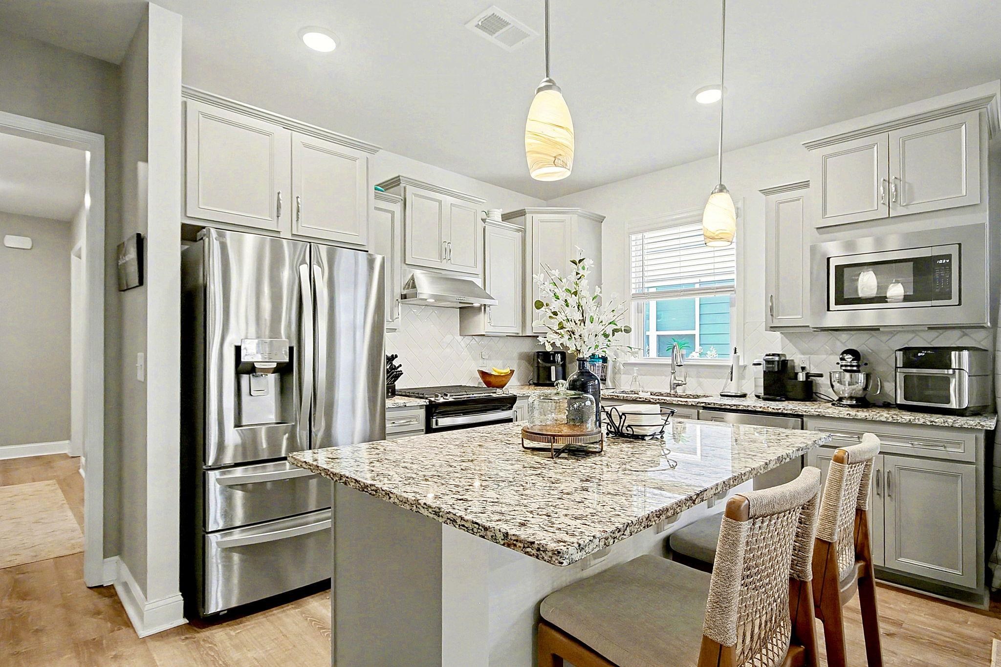 5830 Cremona Drive Myrtle Beach, SC 29577 - Photo 10 of 39 Kitchen featuring appliances with stainless steel finishes, light stone counters, light wood-style floors, a center island, and decorative light fixtures