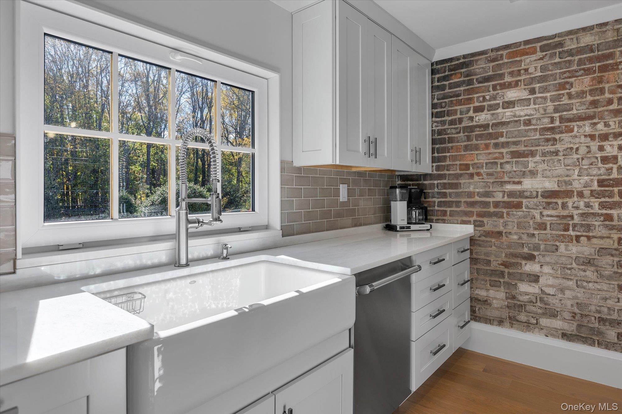 22 Fort Salonga Road Centerport, NY 11721 - Photo 16 of 42 Kitchen with exposed brick wall, white cabinets, light stone counters, and stainless steel dishwasher