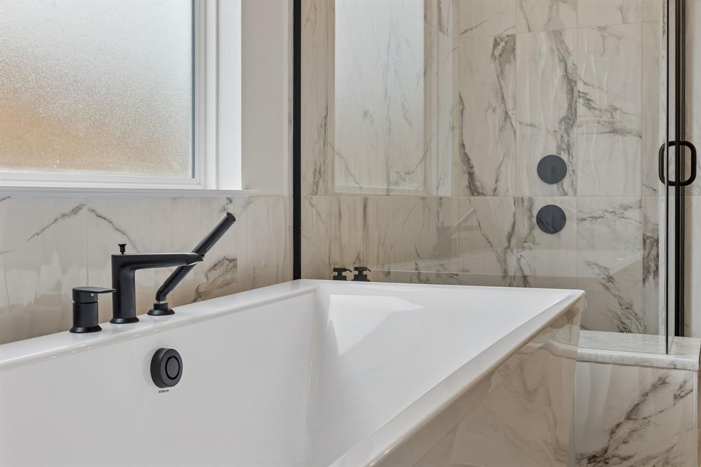 460 Harrison Lane Prosper, TX 75078 - Photo 22 of 40 Built-in soaking tub with matte black fixtures, surrounded by large format tile with natural stone veining, and a frameless glass shower enclosure