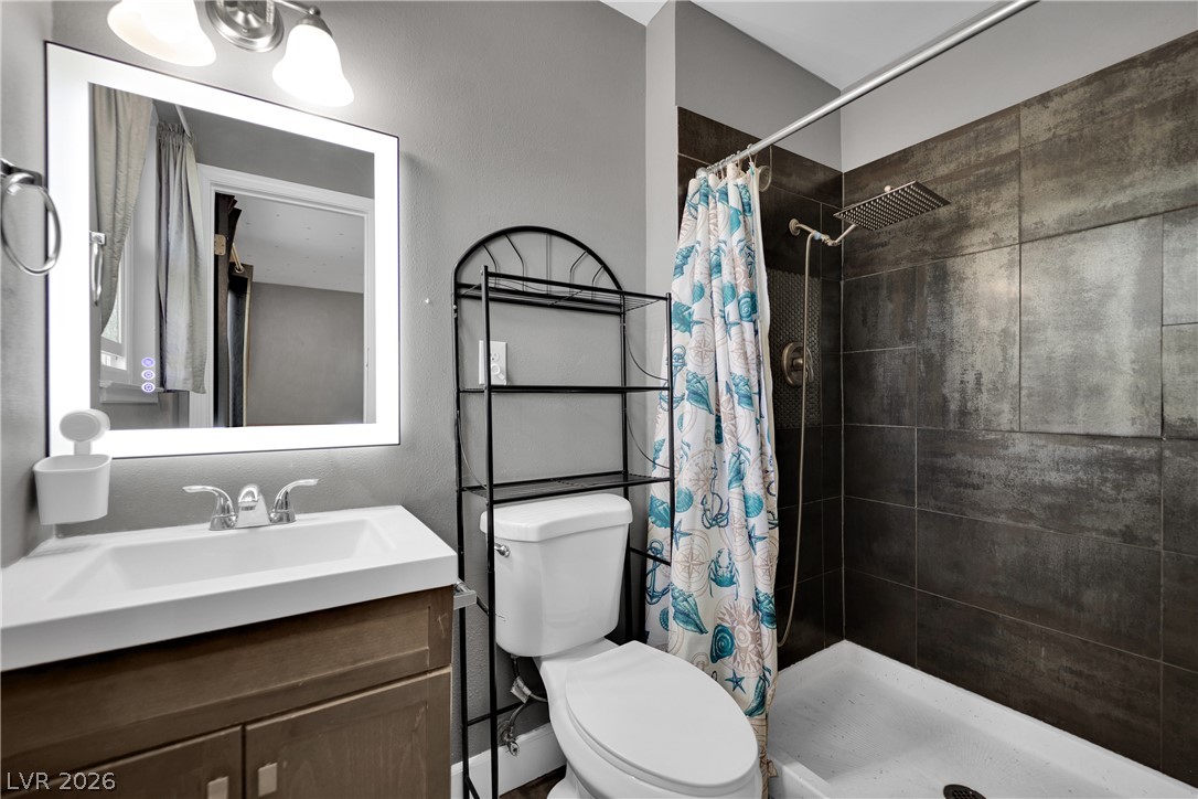 2221 Englestad Street North Las Vegas, NV 89030 - Photo 19 of 32 A well-appointed bathroom features a modern vanity with a lighted mirror and a sleek shower with dark tiled walls.