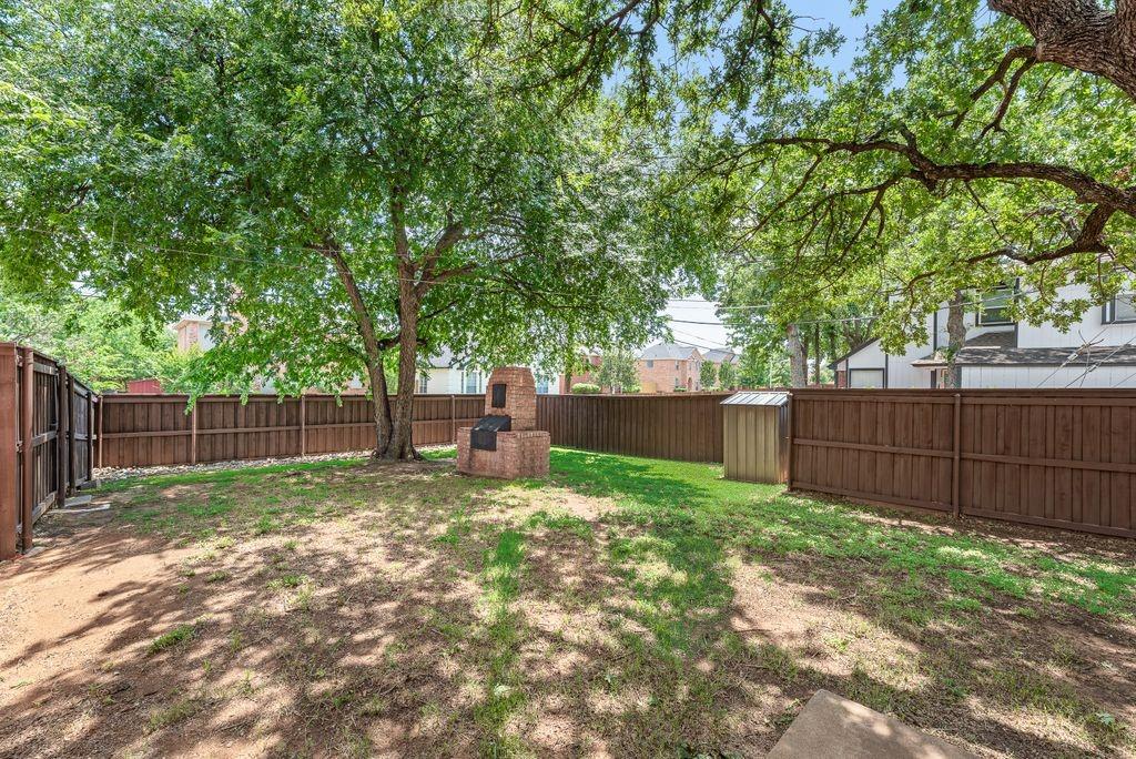 5610 Eagle Rock Road Arlington, TX 76017 - Photo 32 of 33 Expansive backyard featuring mature trees, a built-in brick grilling station, wood privacy fencing, and a storage shed