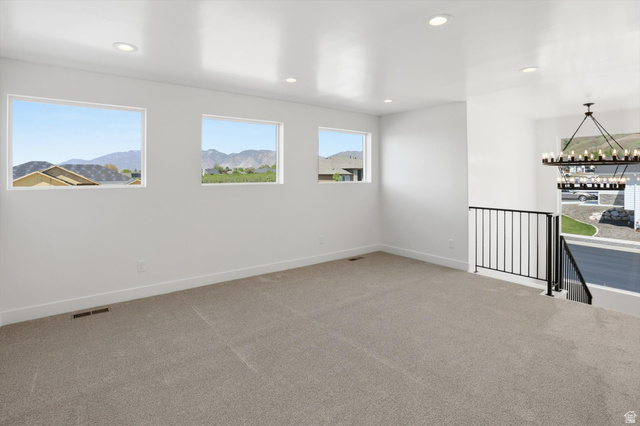 1315 West 3200 South, Unit 17 Perry, UT 84302 - Photo 27 of 58 Spacious upper-level room featuring three rectangular windows, light gray carpeting, recessed ceiling lighting, a dark metal railing, and a multi-tiered chandelier