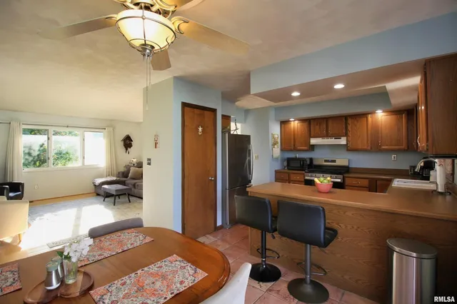 a kitchen with stainless steel appliances granite countertop a stove a refrigerator a sink a dining table and chairs with wooden floor