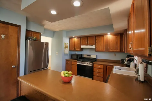 a kitchen with stainless steel appliances a sink a stove a refrigerator cabinets and a dining table