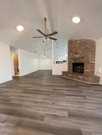 an empty room with wooden floor a ceiling fan a fireplace and entryway