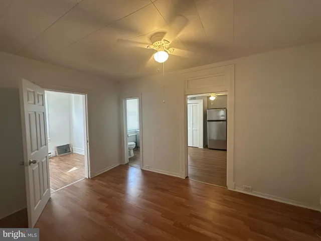 a view of an empty room with wooden floor and a ceiling fan