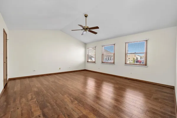 an empty room with wooden floor ceiling fan and windows
